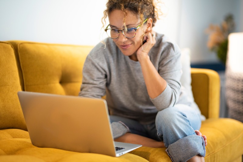 A woman sits on a couch while using a laptop